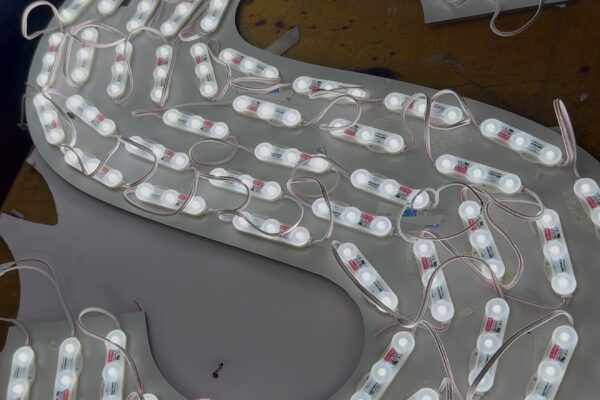 Capital Arts Signage Fabrication – LED Module Backplate Wiring Internal view of a custom 3D letter backplate heavily lined with illuminated white LED modules and wiring during assembly in the Capital Arts workshop.