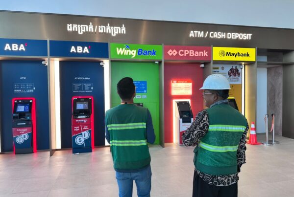 Capital Arts team members inspecting multi-bank ATM signage including ABA, Wing Bank, CPBank, and Maybank installed at a commercial location.