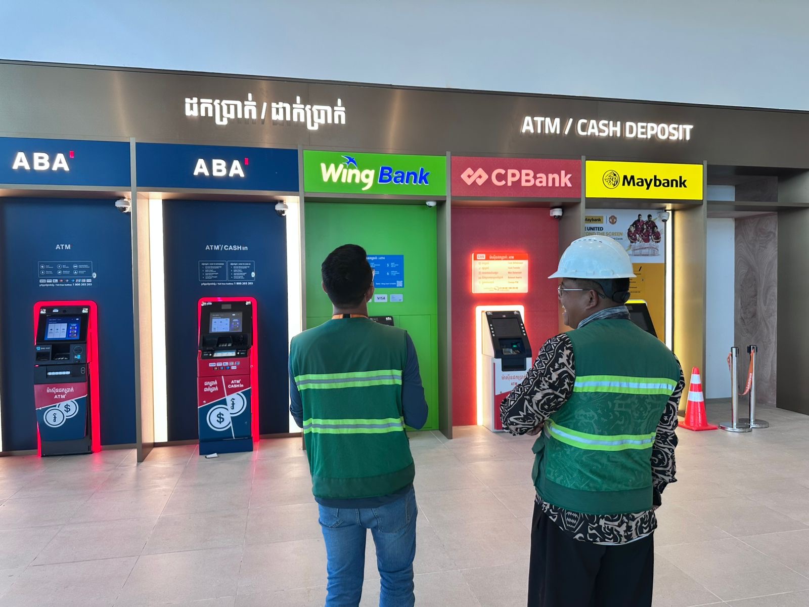 Capital Arts team members inspecting multi-bank ATM signage including ABA, Wing Bank, CPBank, and Maybank installed at a commercial location.
