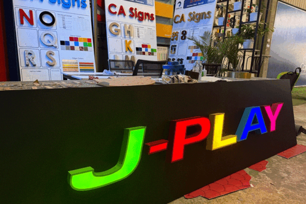 capital-arts-finished-signage-in-workshop Vibrant multi-colored illuminated 3D letters spelling J-PLAY displayed in Capital Arts signage workshop.