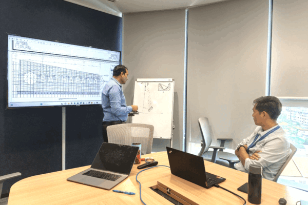 capital-arts-managing-director-sathapana-signage-review Capital Arts Managing Director Mario Yahya explaining facade signage blueprints and whiteboard diagrams to the Sathapana team during a manufacturing meeting.